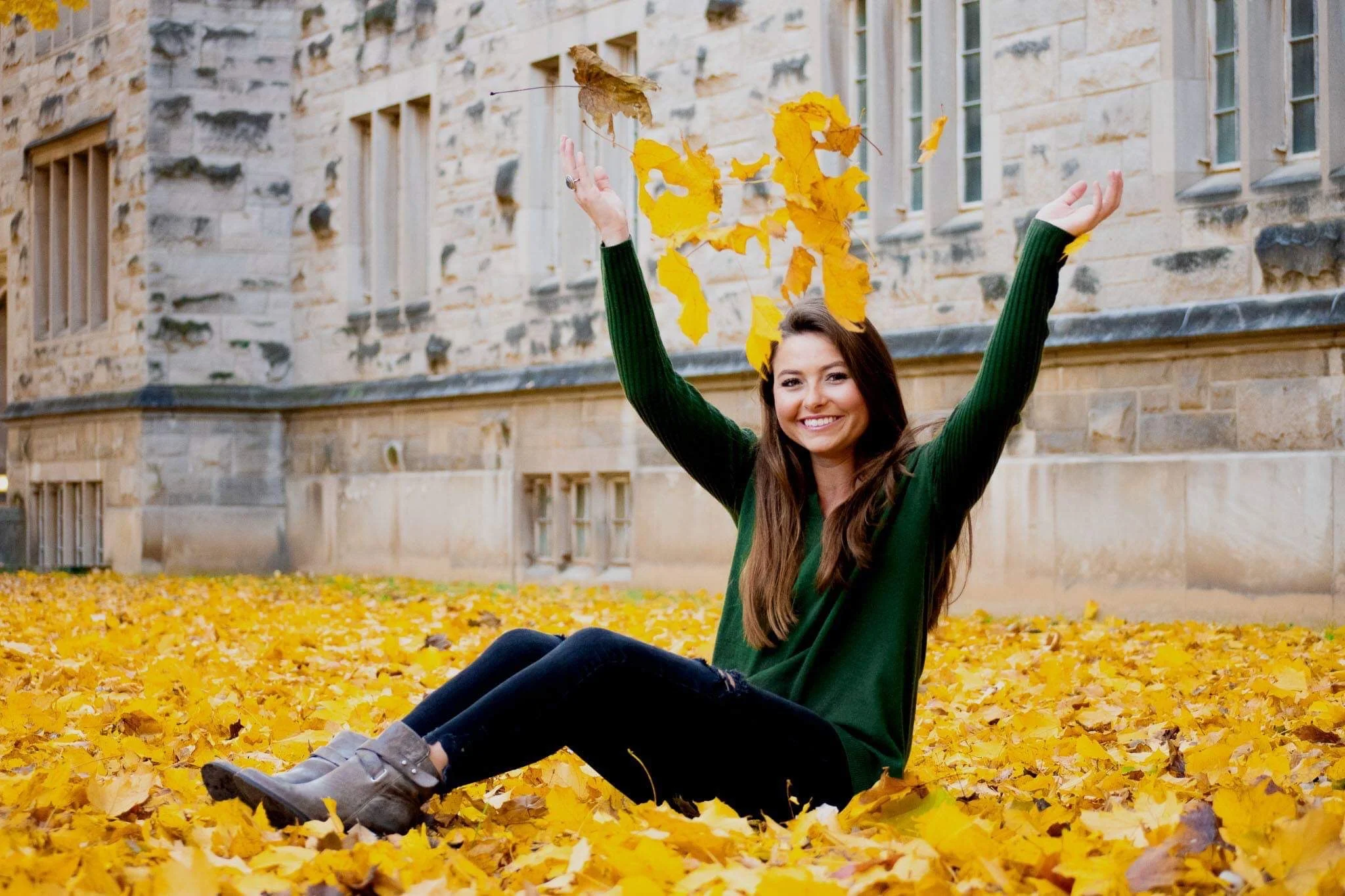 Lauren Dauk sitting in autumn leaves, throwing leaves playfully